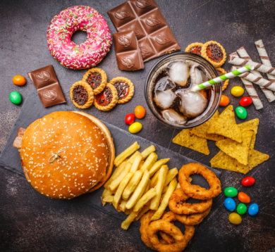 Vielfältige Auswahl an Junkfood mit Burger, Süßigkeiten und Softdrink auf dunklem Hintergrund.