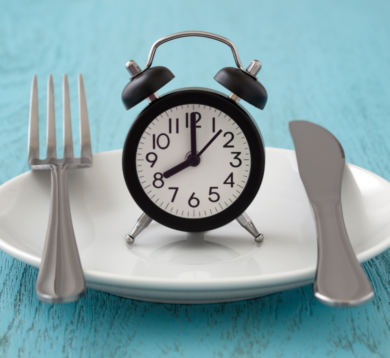 Wecker auf einem Teller zwischen Besteck symbolisiert Essenszeit oder Fastenkonzept.